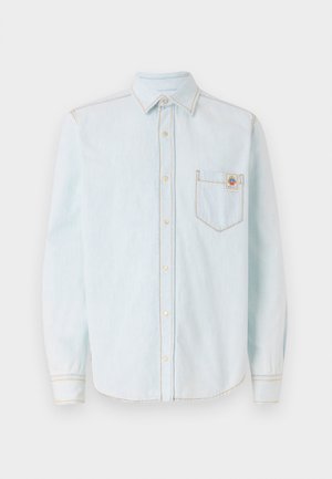 Svetlo modra srajca z dolgimi rokavi iz mehkega denim materiala, ki ima ovratnik s gumbi, žep na prsih in kontrastne rumene šive.