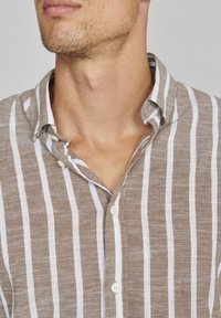 Lichtbruine en witte gestreepte overhemd met kraag, gemaakt van een gestructureerde stof met knoopsluiting en zichtbare stiksels langs de randen.