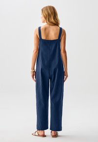 Marineblauer, ärmelloser Overall mit quadratischem Rückenausschnitt und weitem Bein. Hergestellt aus strukturiertem Stoff, mit lockerem Sitz und unauffälligen Nähten.