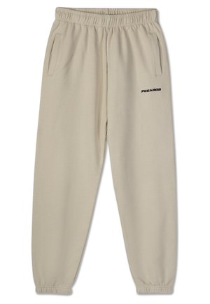 Bežad trennkostüüm, millel on elastne vöökoht, kaks küljetaskut ja must "PEGADOR" logo trükituna vasakul jalal. Sile kangastekstuuri.