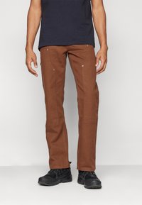 Brown pants with a straight-leg fit, made of a durable fabric. Features visible stitching and metal rivets. Paired with black shoes.