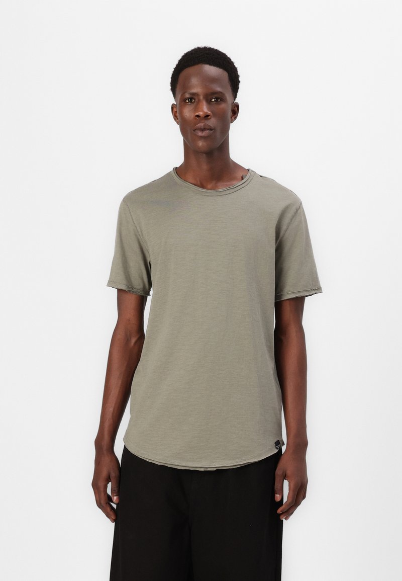 Olivgrünes T-Shirt mit kurzen Ärmeln, rundem Ausschnitt, leicht abgerundetem Saum, rohen Kanten und einem kleinen Logo an der Seite.