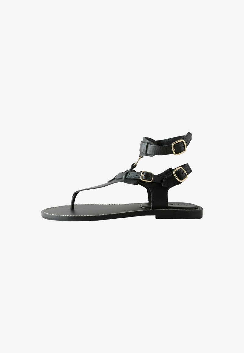 Sandales en cuir noir à lanière, dotées de deux brides réglables avec boucles, semelle plate et surpiqûres contrastées le long des bords.