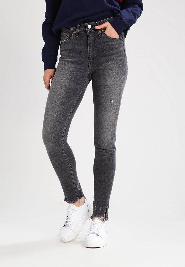 Vaqueros de mezclilla gris de talle alto con corte ajustado, detalles desgastados y dobladillos deshilachados en los tobillos, combinados con zapatillas blancas.