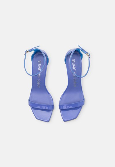 Sandales en cuir verni bleu avec un bout carré, une fine lanière aux chevilles et un talon plat. Semelle intérieure texturée avec le nom de la marque embossé en or.