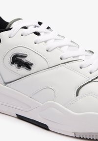 Hvite lær sneakers med svarte detaljer og et teksturert krokodillelogo. Har flate hvite snøringer og polstret krage for komfort.