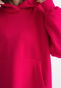 Fuchsia hoodie gemaakt van zacht, glad materiaal met een buidelzak, geribbelde manchetten en een capuchon met trekkoord, met een losse pasvorm.