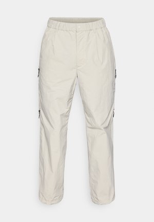 Lightweight, beige cargo pants with an elastic waistband, side zippers, and a smooth texture, featuring a relaxed, straight-fit design.