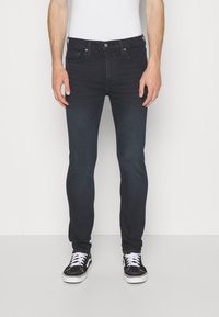 Jeans ajustados de mezclilla en azul oscuro, con un diseño clásico de cinco bolsillos y un cierre de cremallera con botón. Combinados con zapatillas negras.