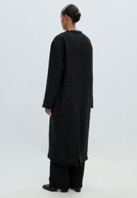 Lange, zwarte tweedjas met rafelige randen, casual pasvorm en textuurpatroon, gecombineerd met bijpassende wijde broek en zwarte laarzen.