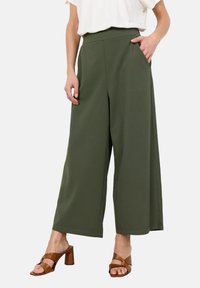 Kalhoty ve stylu culottes z olivově zelené látky, vysoký pas s bočními kapsami, kombinované s hnědými sandály na blokovém podpatku a bílým topem.