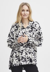 Bluza s cvjetnim uzorkom u crnoj i bijeloj boji, s dizajnom na kopčanje, dugim rukavima i blago labavim krojem. Mekana tkanina s teksturiranim izgledom.