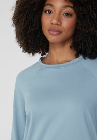 Světle modrý dlouhý rukáv top s kulatým výstřihem, měkká tkanina a raglánové rukávy. Hladká struktura s minimálními akcentovými detaily.