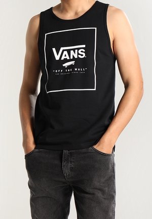 Musta, hihaton puuvillainen toppi, jossa valkoinen "VANS"-logo ja "OFF THE WALL" -teksti, rento istuvuus ja pyöreä pääntie.