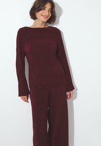 Top lungo a maniche -pleated- bordeaux con scollatura quadrata abbinato a pantaloni ampi dello stesso colore, caratterizzati da una superficie testurizzata e una vestibilità comoda.