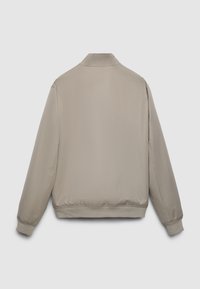 Giacca bomber beige con una texture liscia, caratterizzata da un colletto alla coreana, polsini ed orlo elasticizzati, che presenta un design minimalista.