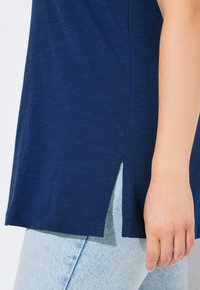 Top blu navy a manica corta con spacco laterale e vestibilità rilassata, realizzato in un tessuto morbido e leggero. Indossato con jeans in lavaggio chiaro.