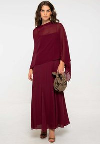 Abito borgogna con maniche in chiffon, silhouette fluida e design stratificato. Abbinato a una borsa marrone a fantasia e tacchi marroni.