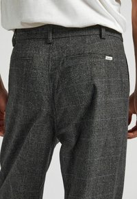 Grå rutiga byxor i en strukturerad tygkvalitet, med bältesloopar, två bakfickor och en liten märkestagg på den högra fickan.