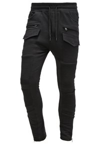 Černé joggingové kalhoty vyrobené z měkké látky, s příčnými ozdobami, zipovými detaily na kotnících a několika předními cargo kapsami.