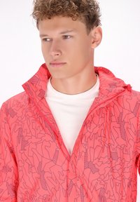 Žiarivo ružová bunda s geometrickým vzorom v tmavšej ružovej farbe. Má vysoký golier a zips, je vyrobená z ľahkého materiálu.