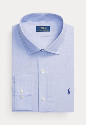 Chemise habillée bleu clair à manches longues, pantalon bleu marine foncé, cravate à motif rouge et sarcelle, mocassins marron, montre décontractée au poignet.