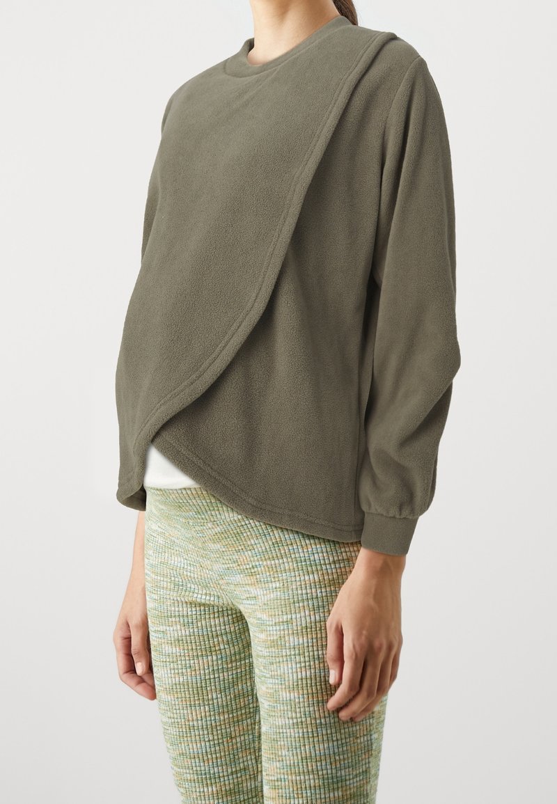 Olivengrøn fleecebluse med draperet design, rund halsudskæring og lange, puffede ærmer, kombineret med teksturerede, mønstrede grønne og gule leggings.