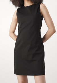 Svart ärmlös klänning med en figurnära siluett, gjord av en slät tyg, med rundad halsringning och knälång fåll. Inga synliga mönster eller accenter.