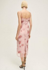 Rochie midi cu imprimeu floral roz, cu bretele subțiri, deschidere pe spate, textură transparentă și siluetă ajustată. Accesorizată cu pantofi cu toc verzi, cu curele.