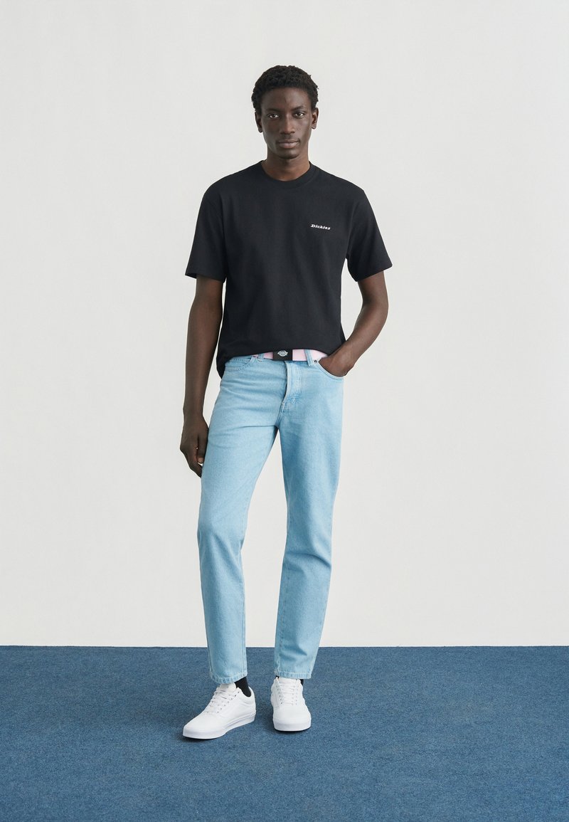 Camiseta negra de algodón, vaqueros de mezclilla azul claro y zapatillas blancas. Diseño simple, forma ajustada, con detalle sutil de logo en la camiseta.