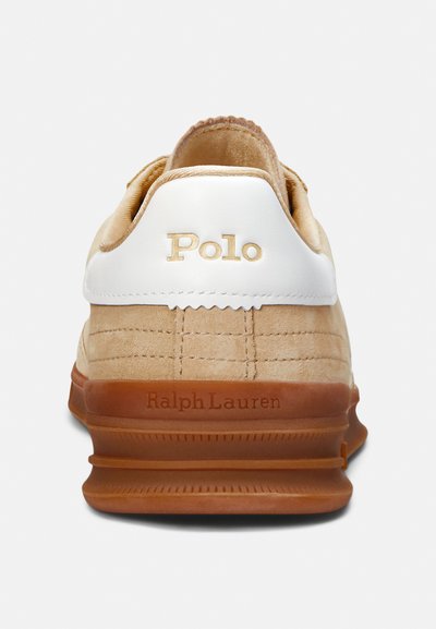 Beige suede sneaker with white leather accents, featuring "Polo" logo in gold and textured rubber sole. Includes stitched detailing on fabric.