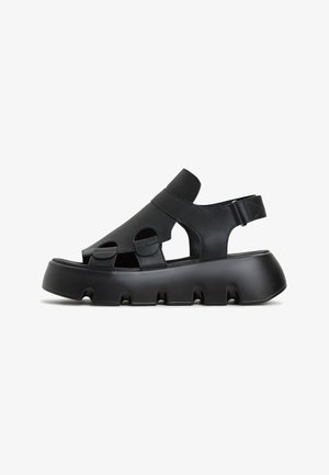 Zwarte leren sandalen met open teen, gebogen ontwerp, verstelbare band en dikke, gevoerde zool met uitsnijdingen.