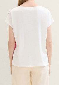 T-shirt bianco in cotone con maniche corte, caratterizzata da un accento rosa sul lato. Vestibilità comoda con scollatura rotonda. Texture liscia.