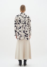 Kreemikas pikkade varrukatega särk musta abstraktse mustriga, millele on lisatud beež seelik. Komplekt on lõdva lõike ja tekstuuriga kangaga.