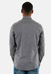 Camisa gris de manga larga con cuello abotonado, tejido texturizado y dobladillo curvado. La vista trasera muestra los puños abotonados y un diseño de hombros sin costuras.