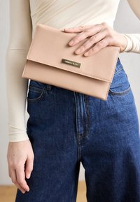 Pochette en cuir rose pâle avec finition texturée et quincaillerie dorée. Présente une forme rectangulaire et une fermeture à rabat.