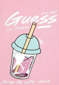 Gaiši rozā krekls ar grafiku, kurā attēlots sulu dzēriens ar tirkīza vāciņu, salmiņu un sekrešu detaļām caurspīdīgā krūzē, ar tekstu "Guess".