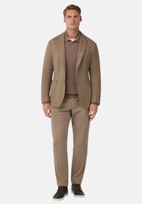 Hnědý blazer s klopami přes hnědý polo triko. Spárováno se světle hnědými kalhotami a tmavými teniskami. Hladká textura, přiléhavý střih.