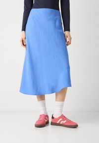 Blå knelengde skjørt med en jevn tekstur og en flytende design, kombinert med rosa joggesko og hvite ankelstrømper.