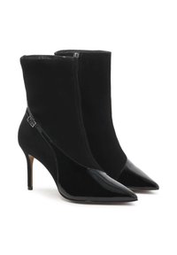 Botines negros con un diseño elegante y punta afilada, fabricados en un material aterciopelado y con detalles de cuero brillante, sobre un tacón de aguja.