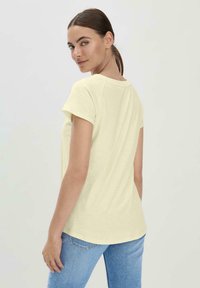 Korte mouwen lichtgele t-shirt met een ronde halslijn, relaxte pasvorm en een gebogen zoom, van de achterkant weergegeven. Materiaal lijkt zacht te zijn.