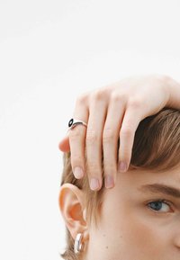 Anillo de plata con una banda delgada, que presenta un acento circular negro. Acabado con una textura suave y un diseño minimalista.