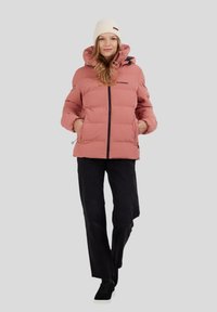 Chaqueta acolchada rosa con capucha, cierre de cremallera, bolsillos laterales y detalles en negro, combinada con pantalones negros de pierna ancha y un gorro color crema.