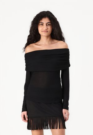 Svart off-shoulder langermet topp med rynket halslinning, paret med en tettsittende svart mini-skjørt med frynse detaljer i kanten.