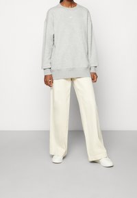 Šedá mikina s kulatým výstřihem a žebrovanými manžetami, doplněná krémovými širokými kalhotami a bílými botami. Na hrudi je viditelné logo Nike.