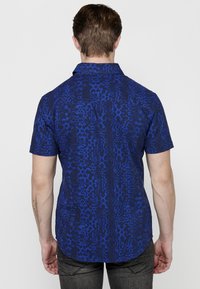 Camicia a maniche corte di colore blu scuro con un motivo astratto e texturizzato. Orlo dritto, colletto con bottoni e una finitura in tessuto liscia.