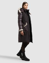 Długa, ciemnofioletowa puchowa kurtka z kapturem wyłożonym futrem, bocznymi kieszeniami i zamkiem błyskawicznym z przodu. Czarne botki za kostkę z teksturowaną podeszwą.