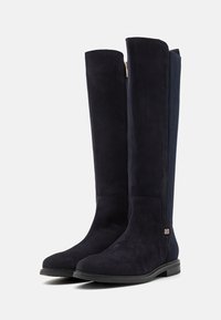 Knähöga, marinblåa mockastövlar med en slät finish, guldzipper, texturerad sidopanel och platt gummisula.