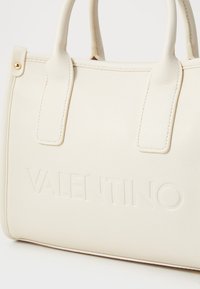Bílá kožená kabelka s vyraženým logem "VALENTINO", dvojitými horními uchy a jemnou texturou. Obsahuje akcenty z pozlaceného kovu.
