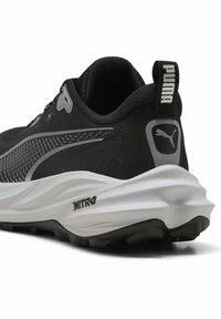 Zapatilla atlética negra con parte superior de malla texturizada, media suela blanca y suela de goma. Presenta una etiqueta con el logotipo de PUMA y acentos gris angulares.